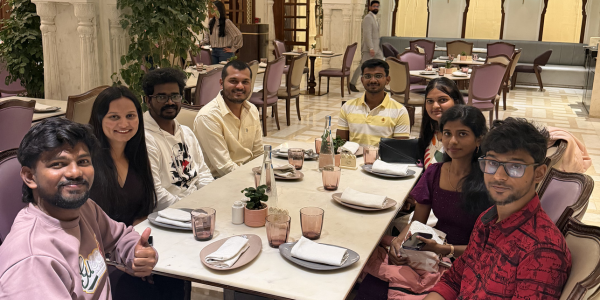 a group of people sat around a table, smiling at the camera