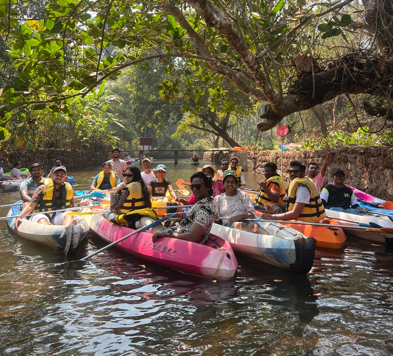 Our India team smiling in colourful kayaks and life jackets on a tree-lined river in Goa on our annual team-building trip