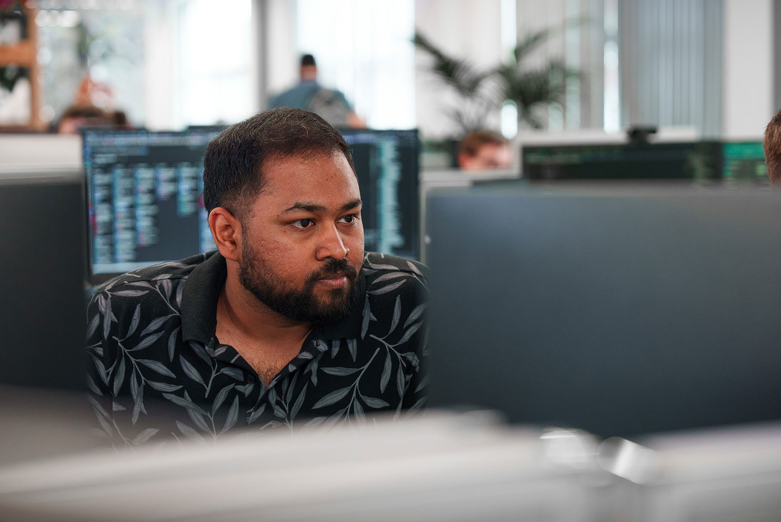 Kalyan Jothimurugan, software engineer at Abstract Group, concentrating on his screen in our open-plan office, with colleagues and code monitors behind
