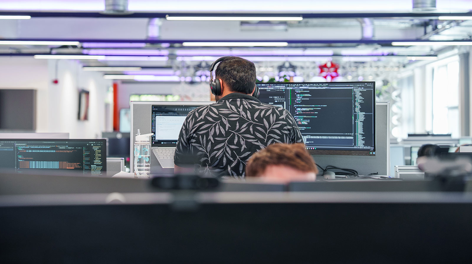 Kalyan Jothimurugan, software engineer, wearing headphones and working on code across two monitors in our open-plan office