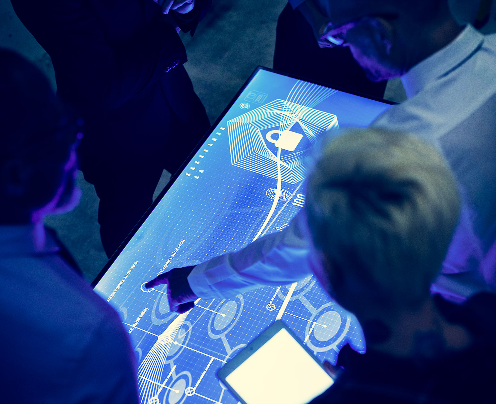 Group gathered around a digital touchscreen table showing a padlock and access control diagram, one person pointing at it